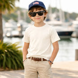 Child wearing off-white tee ,sunglasses and a cap by a waterfront