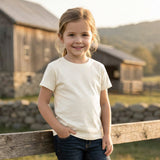 Young girl standing by a wooden fence with a barn and mountains in the background