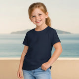 Young girl wearing a navy blue t-shirt and jeans standing on a beach.