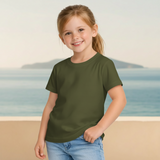 Young girl wearing an olive green t-shirt and blue jeans standing on a beach.
